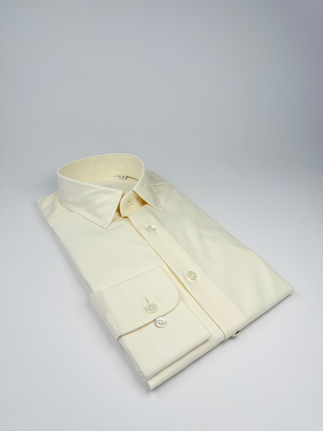 Folded cream-colored dress shirt on a light gray background