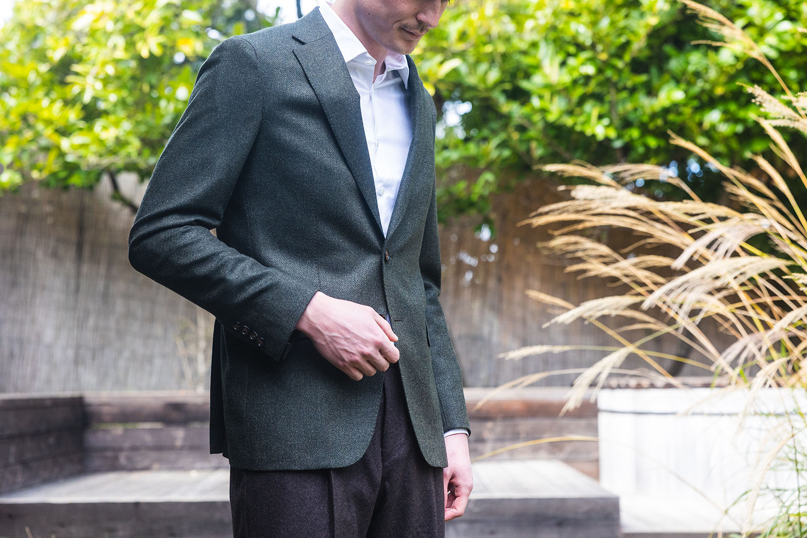 Man wearing a green blazer and white shirt outdoors with plants in the background
