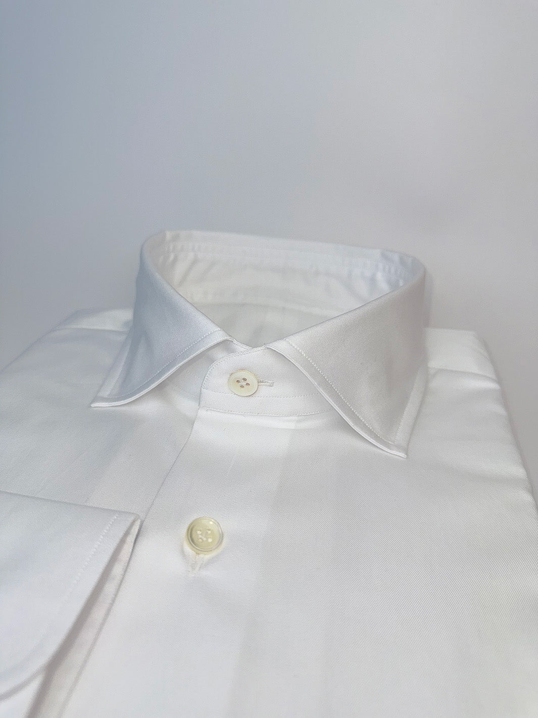 Close-up of a white shirt collar with buttons on a light gray background