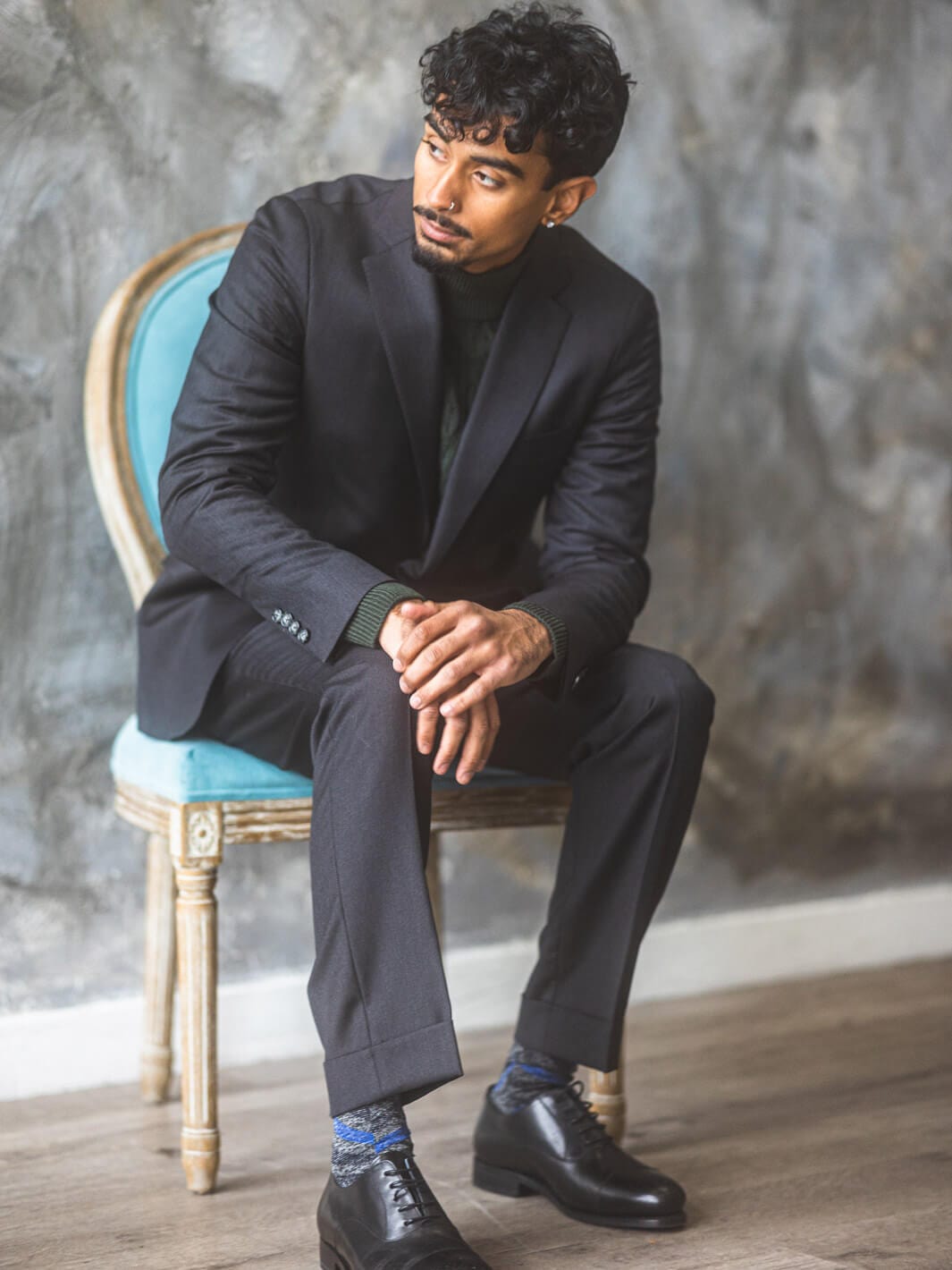 Picture of man sitting on emerald chair wearing Anatoly & Sons charcoal natural stretch suit